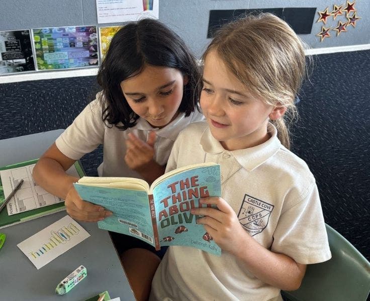 Two female students are sharing the same book and reading together.