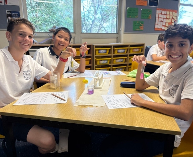 Three male students are smiling at the camera as they each hold a test tube.
