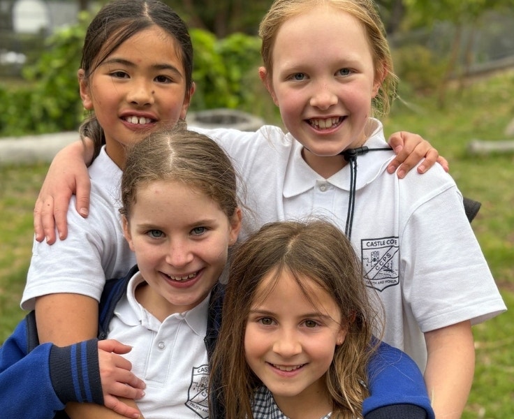 Four female students are staring at the camera and smiling as they have their arms around each other.