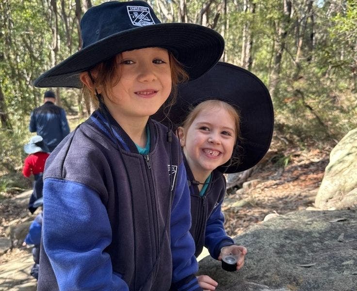 Two Kindergarten students standing in the bush and smiling at the camera.