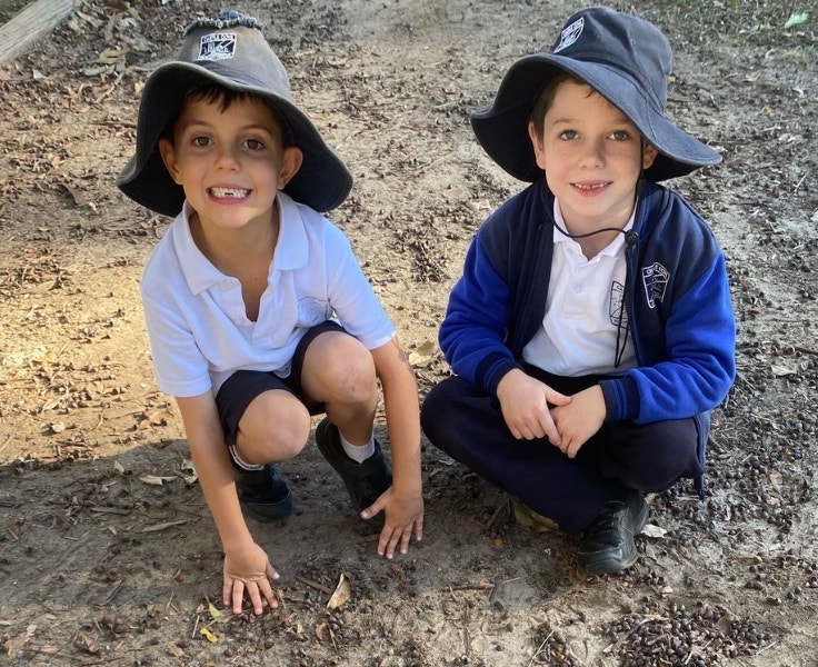 Two male students sitting in sand and smiling up at the camera.