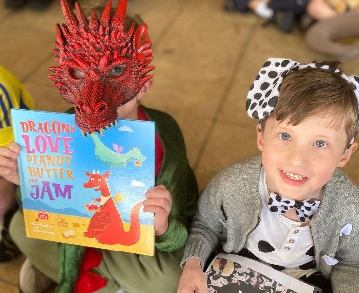 One student wearing a red dragon mask holding a book that says