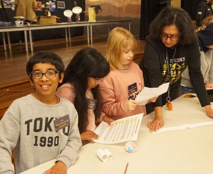 Male student smiling at the camera while two female students each read a piece of paper with a teacher.