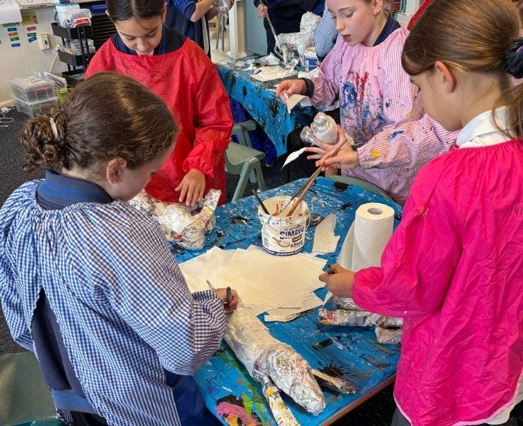 Four female students are wearing art smocks and painting paper mache dogs.