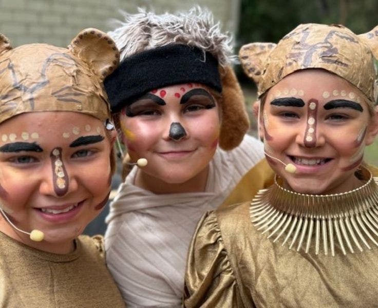 Three female students are smiling at the camera. They are wearing Lion King-inspired costumes.