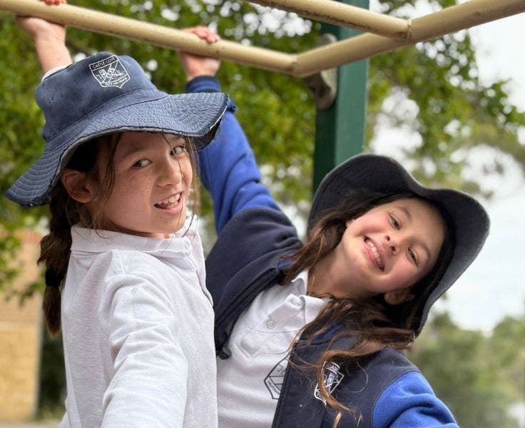 Two female students holding on the monkey bars with one hand and smiling at the camera.