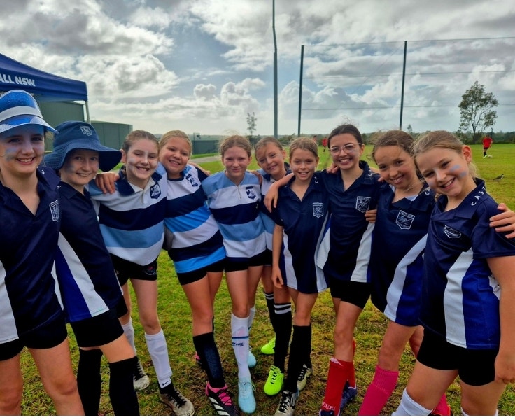 A line of female students with their arms around each others' backs. They are wearing different blue sports jerseys.